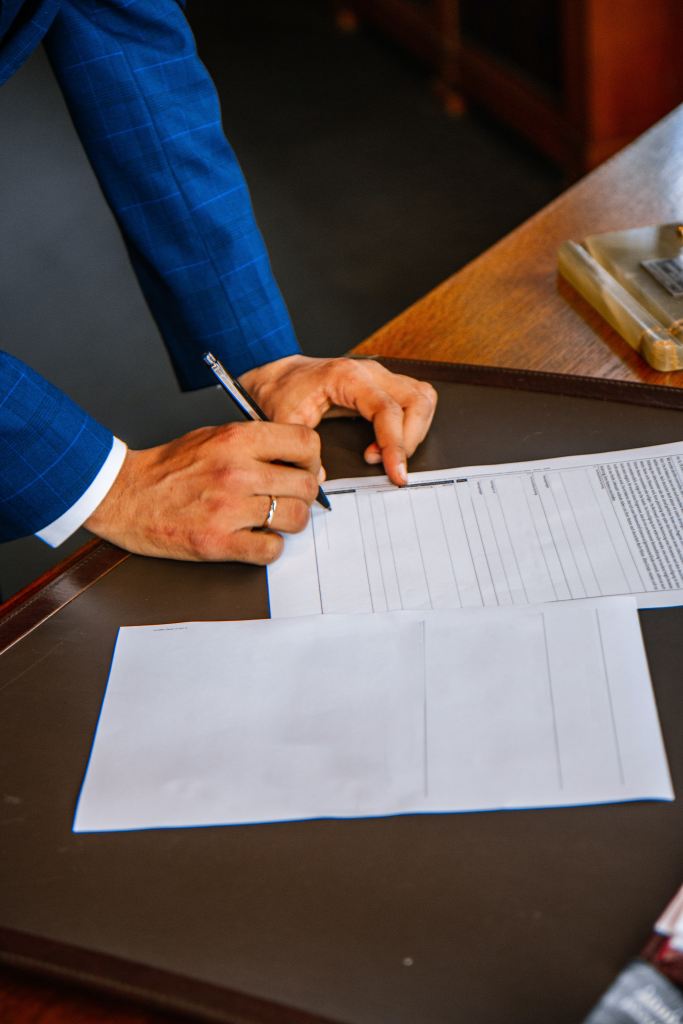 A closeup of a professional man's hands signing a set of documents with a black pen.