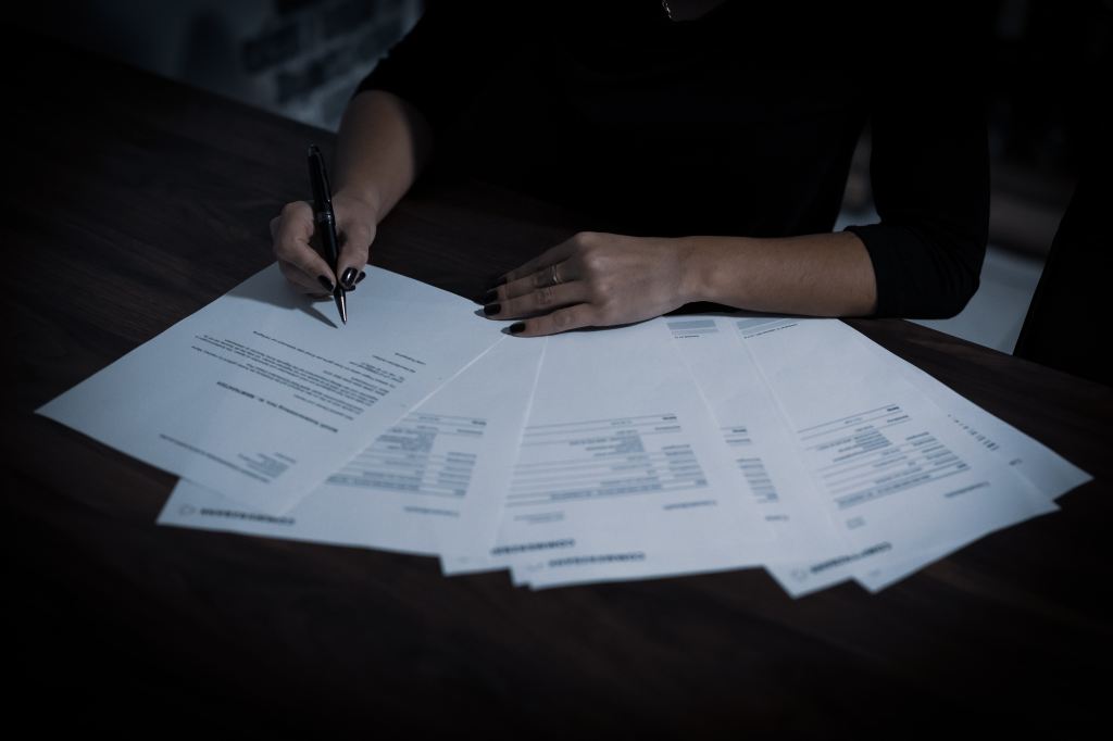 A silhouetted image of a woman wearing a dark blouse with her hands highlighted and signing a group of documents.